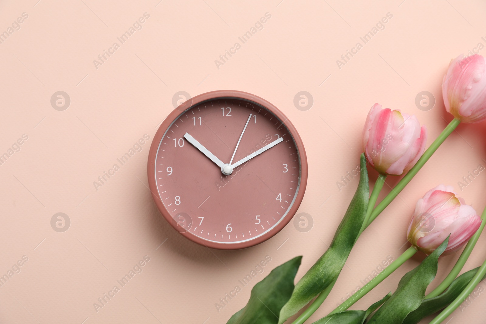 Photo of Menopause. Alarm clock and tulips on beige background, flat lay