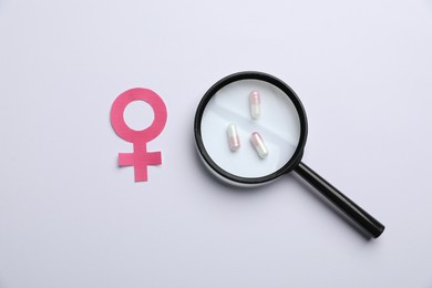 Photo of Menopause. Female gender symbol and magnifying glass over pills on light background, flat lay