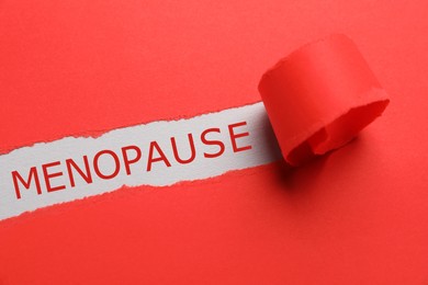 Photo of Word Menopause on light background, view through hole in torn red paper