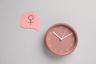 Photo of Menopause. Female gender symbol and alarm clock on light grey background, flat lay
