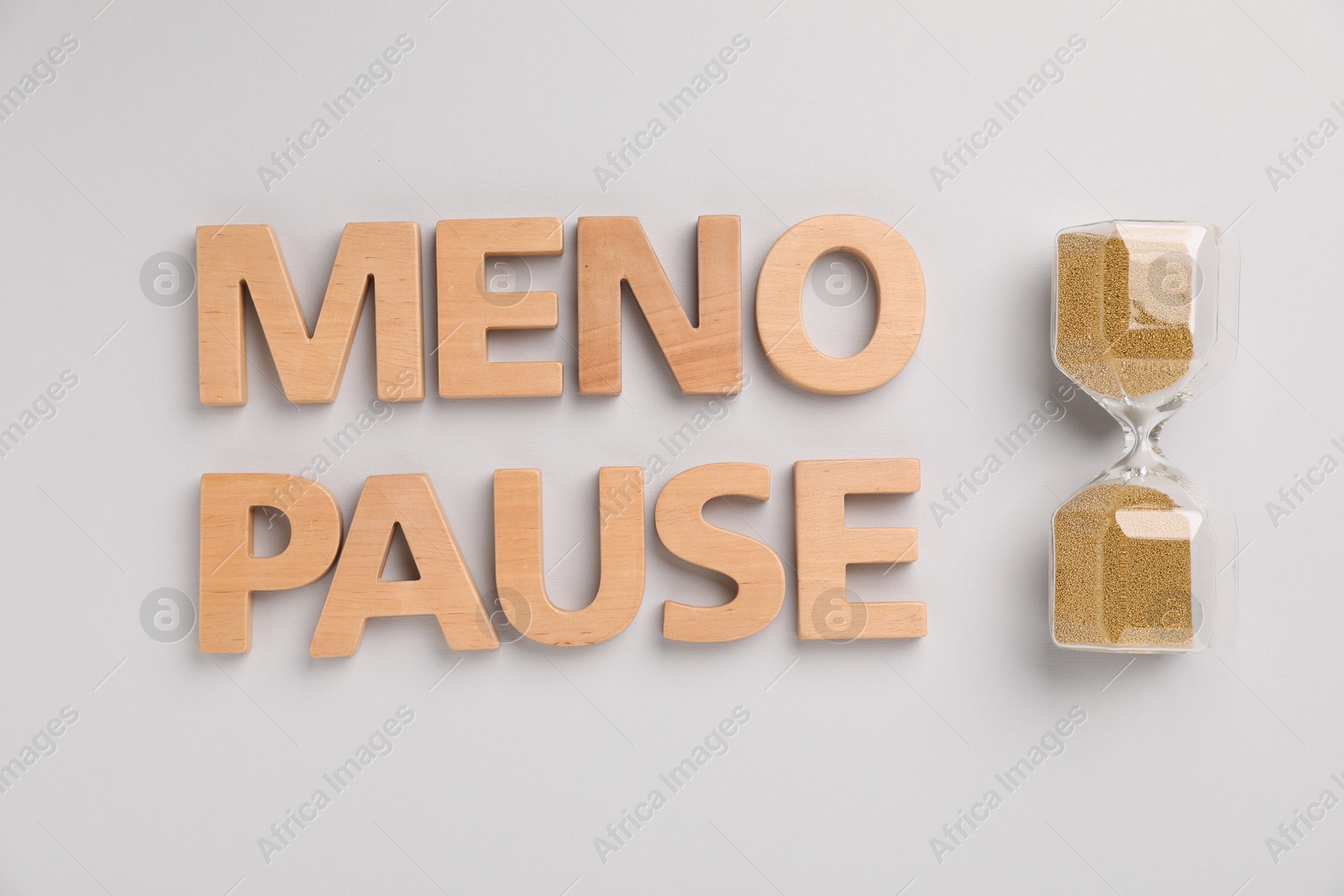 Photo of Word Menopause and hourglass on light grey background, top view
