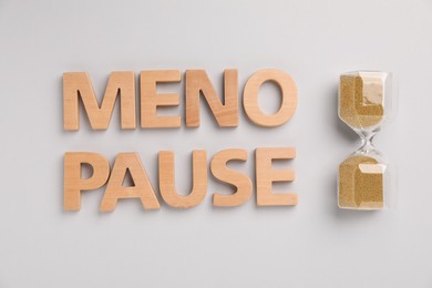 Photo of Word Menopause and hourglass on light grey background, top view