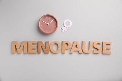 Photo of Word Menopause, alarm clock and female gender symbol on light grey background, flat lay