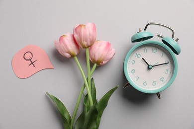 Photo of Menopause. Female gender symbol, alarm clock and tulips on light grey background, flat lay