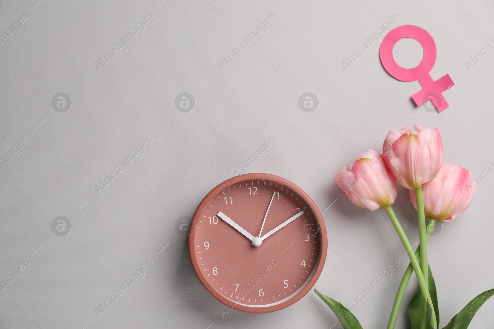 Photo of Menopause. Female gender symbol, alarm clock and tulips on light grey background, flat lay. Space for text