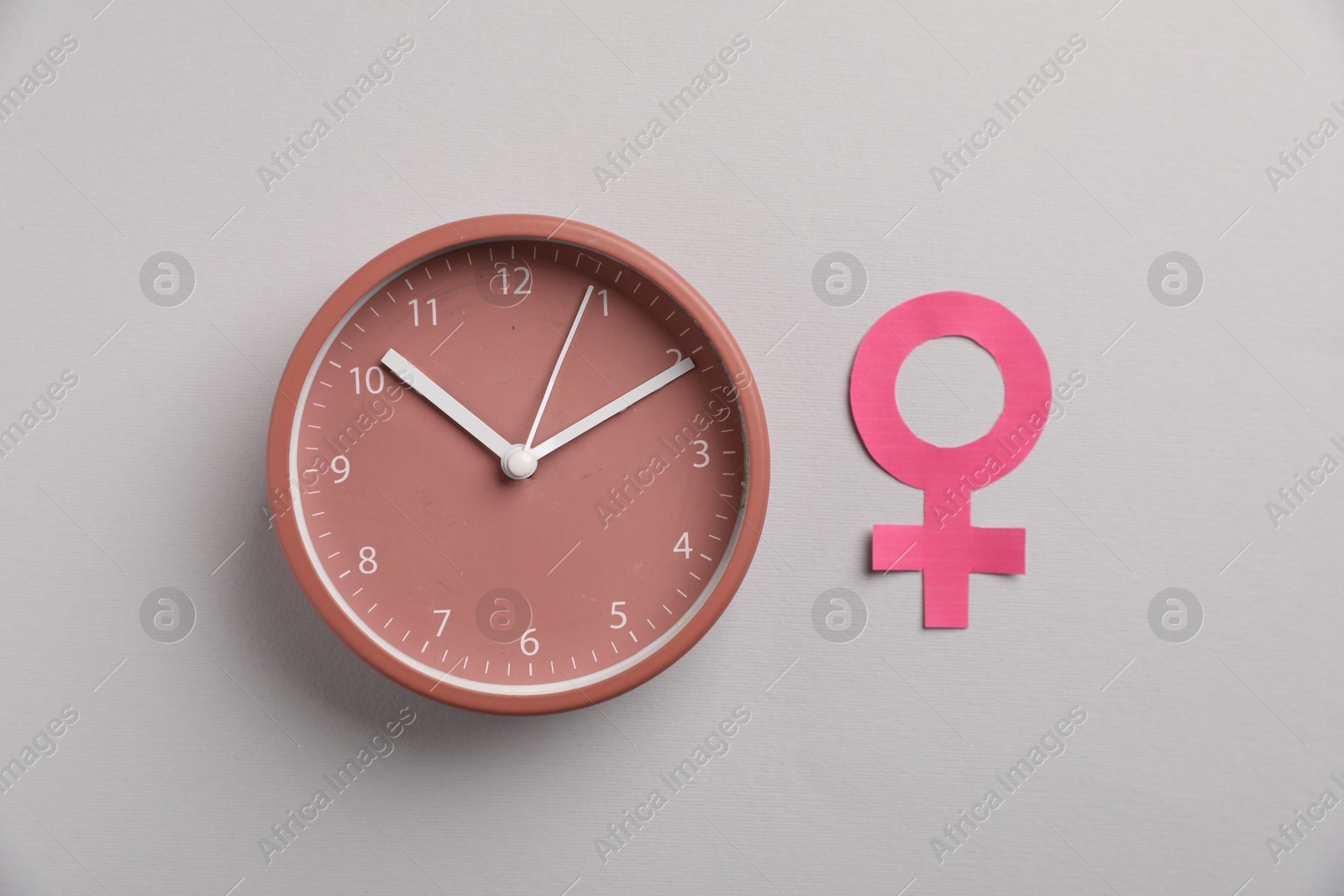Photo of Menopause. Female gender symbol and alarm clock on light grey background, flat lay