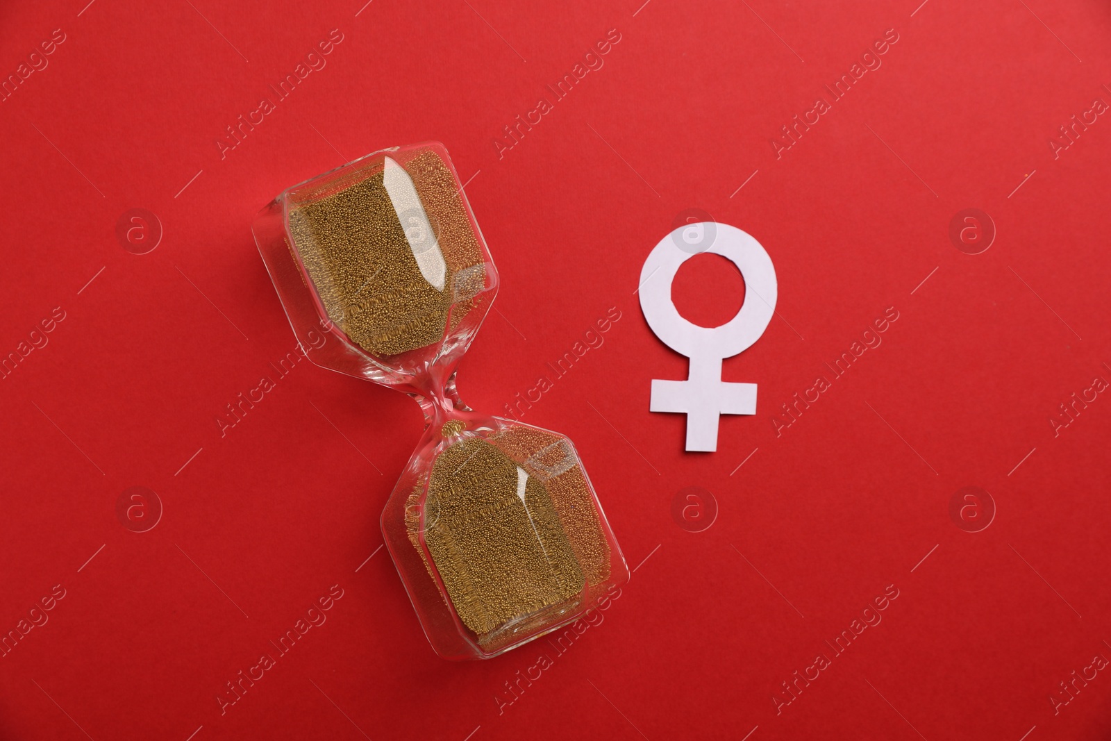 Photo of Menopause. Female gender symbol and hourglass on red background, top view