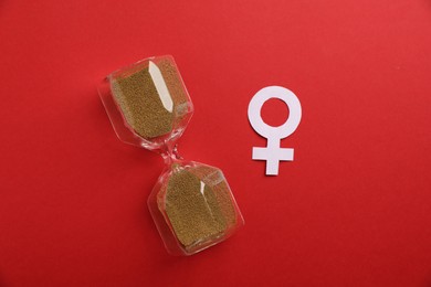 Photo of Menopause. Female gender symbol and hourglass on red background, top view