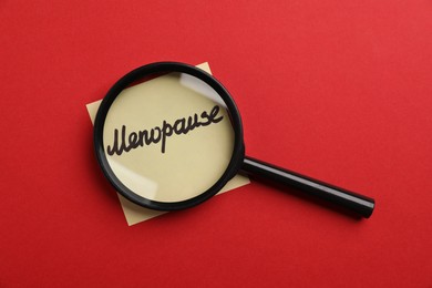 Photo of Magnifying glass over paper note with word Menopause on red background, top view