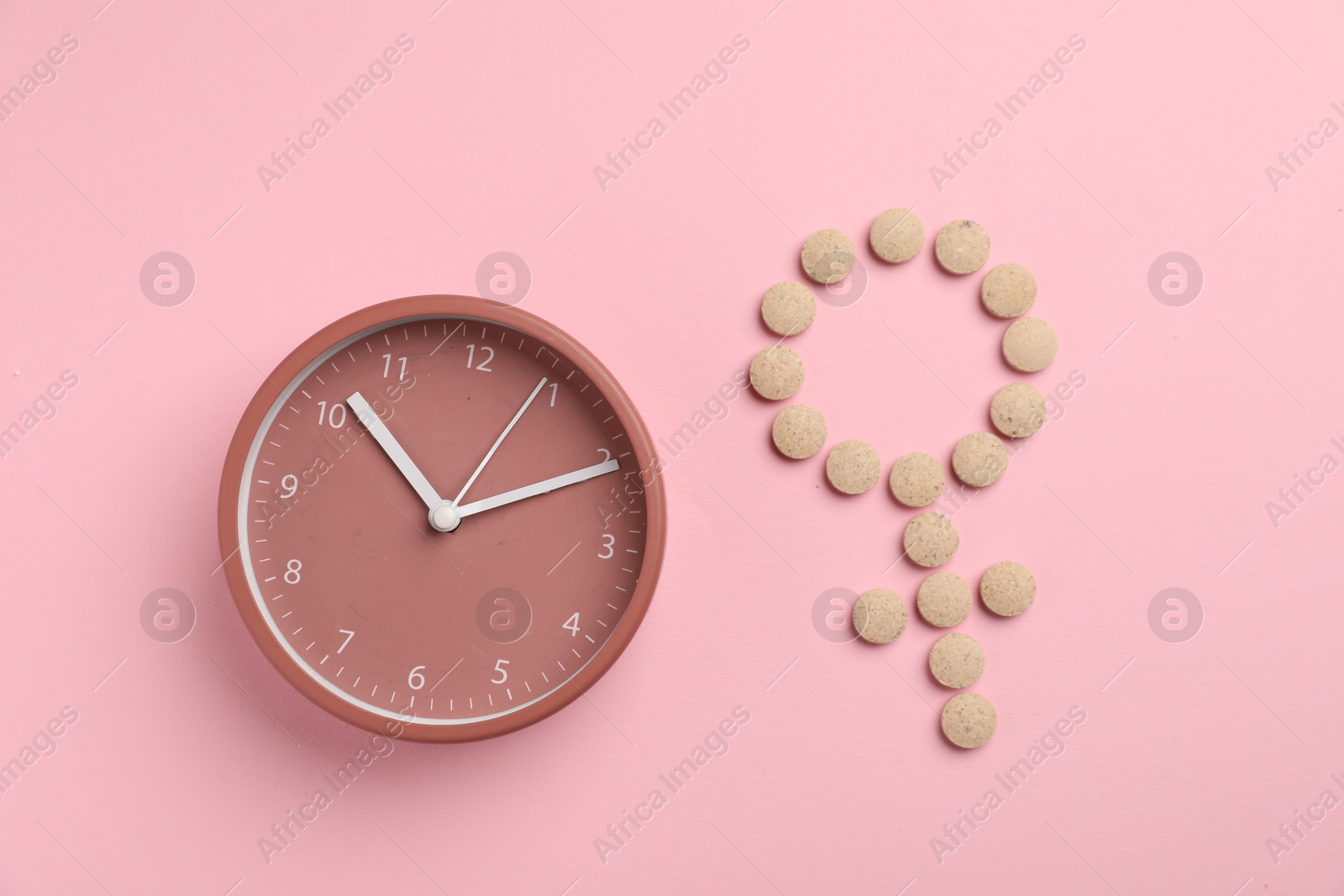 Photo of Menopause. Female gender symbol made with pills and alarm clock on pink background, top view