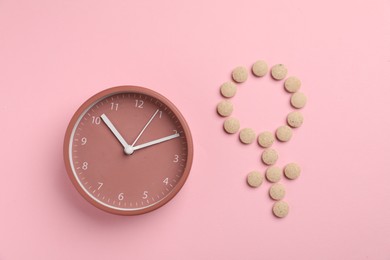 Photo of Menopause. Female gender symbol made with pills and alarm clock on pink background, top view