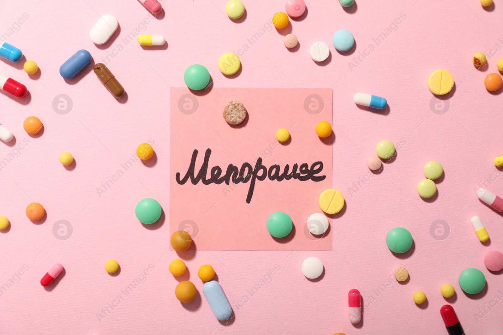 Photo of Paper note with word Menopause and pills on pink background, flat lay