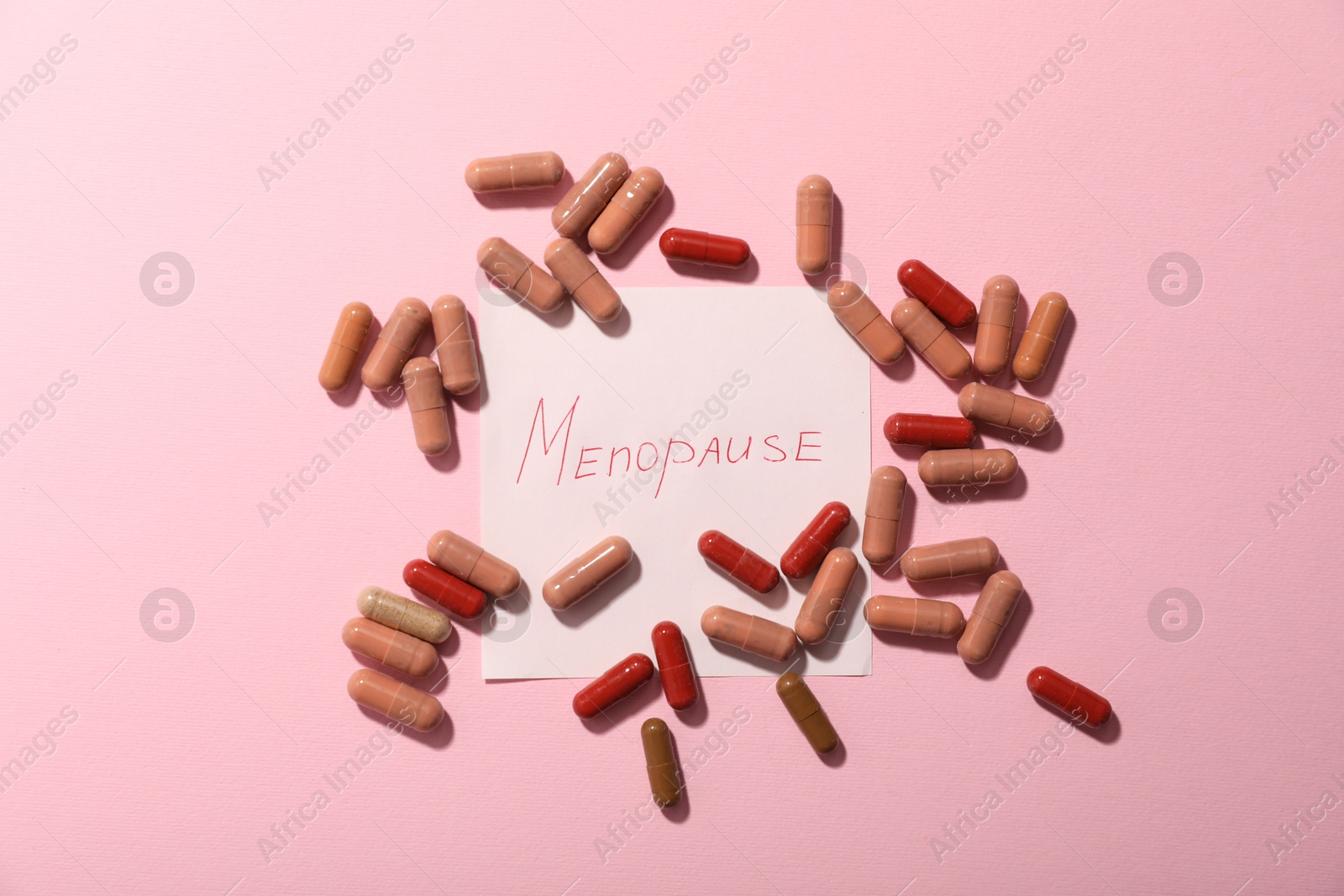 Photo of Paper note with word Menopause and pills on pink background, flat lay