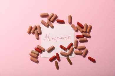 Photo of Paper note with word Menopause and pills on pink background, flat lay