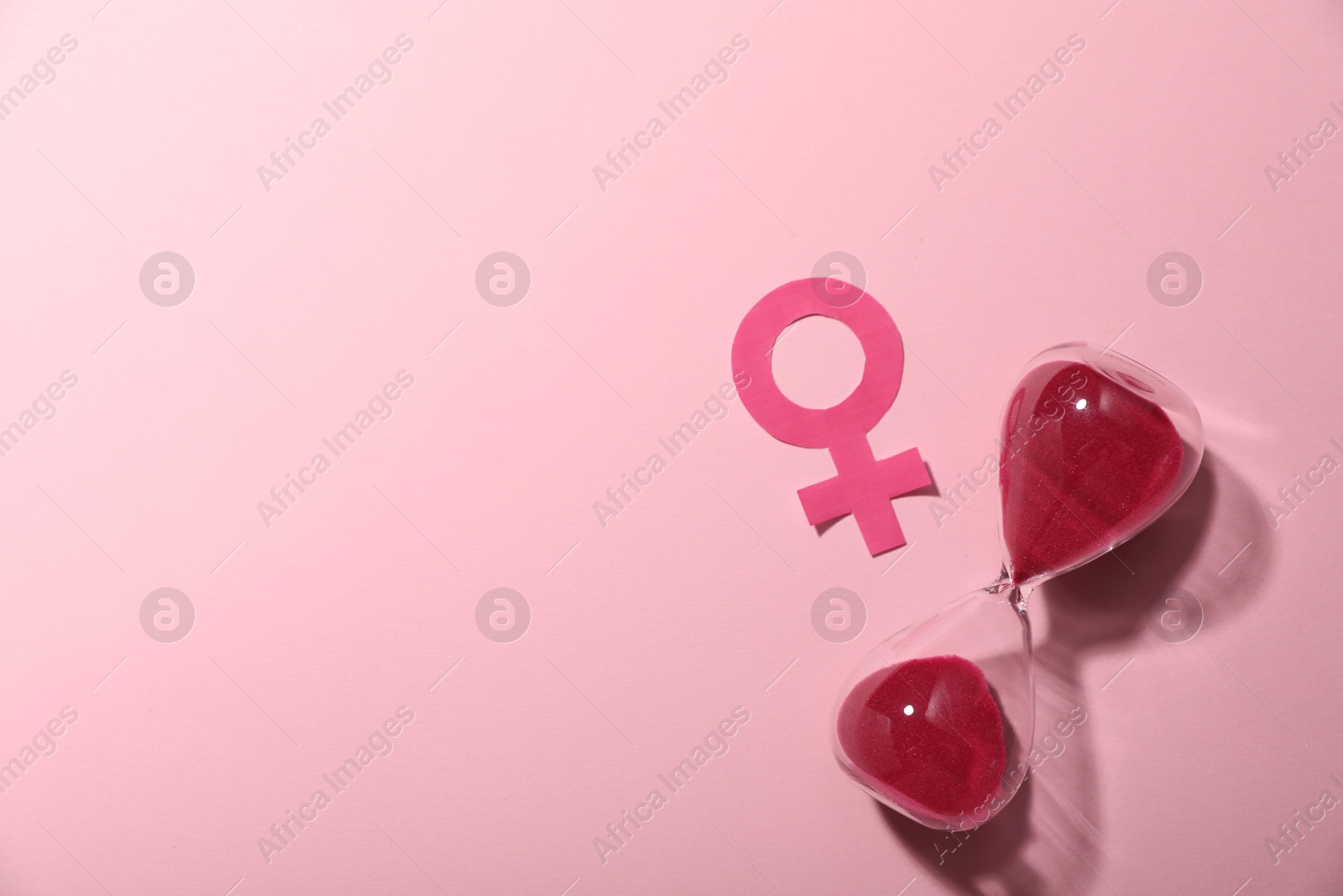 Photo of Menopause. Female gender symbol and hourglass on pink background, top view. Space for text