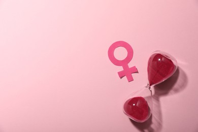 Photo of Menopause. Female gender symbol and hourglass on pink background, top view. Space for text
