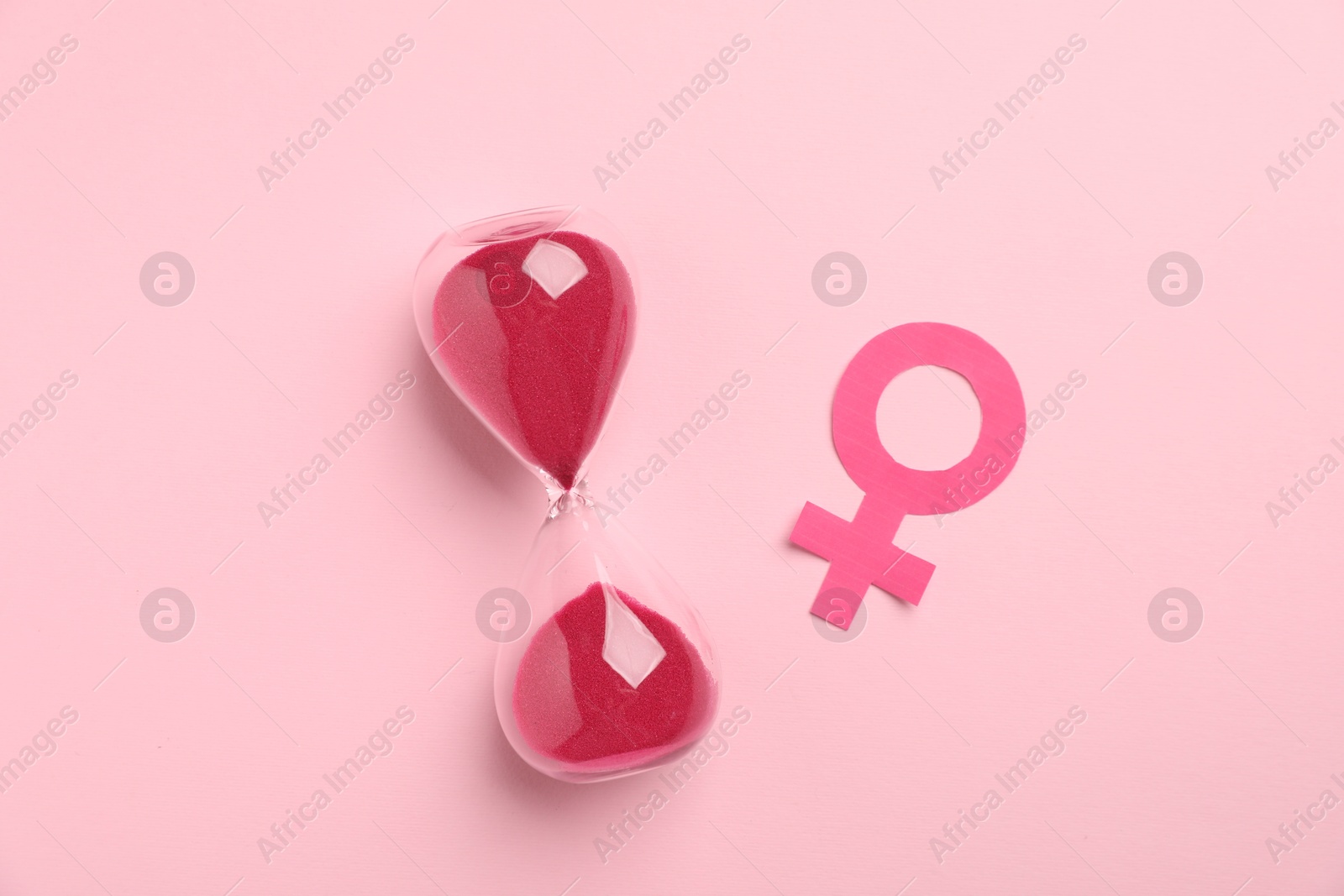 Photo of Menopause. Female gender symbol and hourglass on pink background, top view