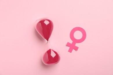 Photo of Menopause. Female gender symbol and hourglass on pink background, top view
