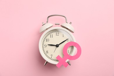 Photo of Menopause. Female gender symbol and alarm clock on pink background, top view