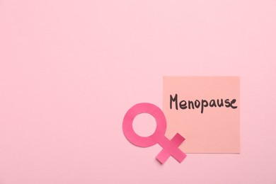 Photo of Paper note with word Menopause and female gender symbol on pink background, top view. Space for text