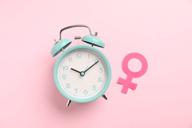 Photo of Menopause. Female gender symbol and alarm clock on pink background, flat lay