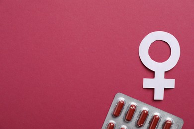 Photo of Menopause. Female gender symbol and pills on crimson background, flat lay. Space for text