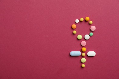 Photo of Menopause. Female gender symbol made with pills on crimson background, top view. Space for text