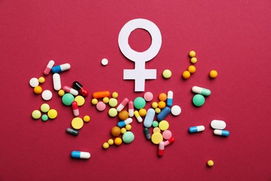 Photo of Menopause. Female gender symbol and pills on crimson background, flat lay