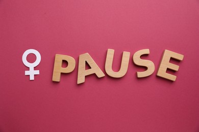 Photo of Word Pause and female gender symbol on crimson background, top view