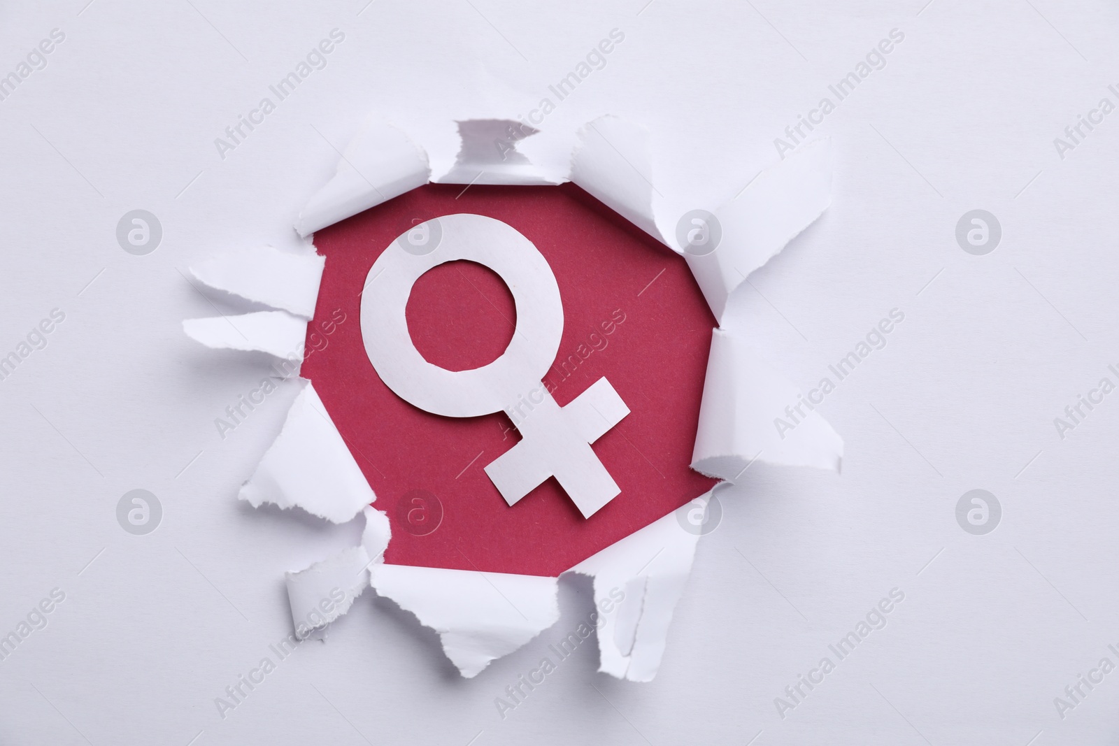 Photo of Menopause. Female gender symbol on crimson background, view through hole in torn white paper