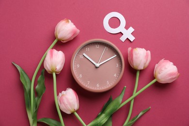 Photo of Menopause. Female gender symbol, alarm clock and tulips on crimson background, flat lay