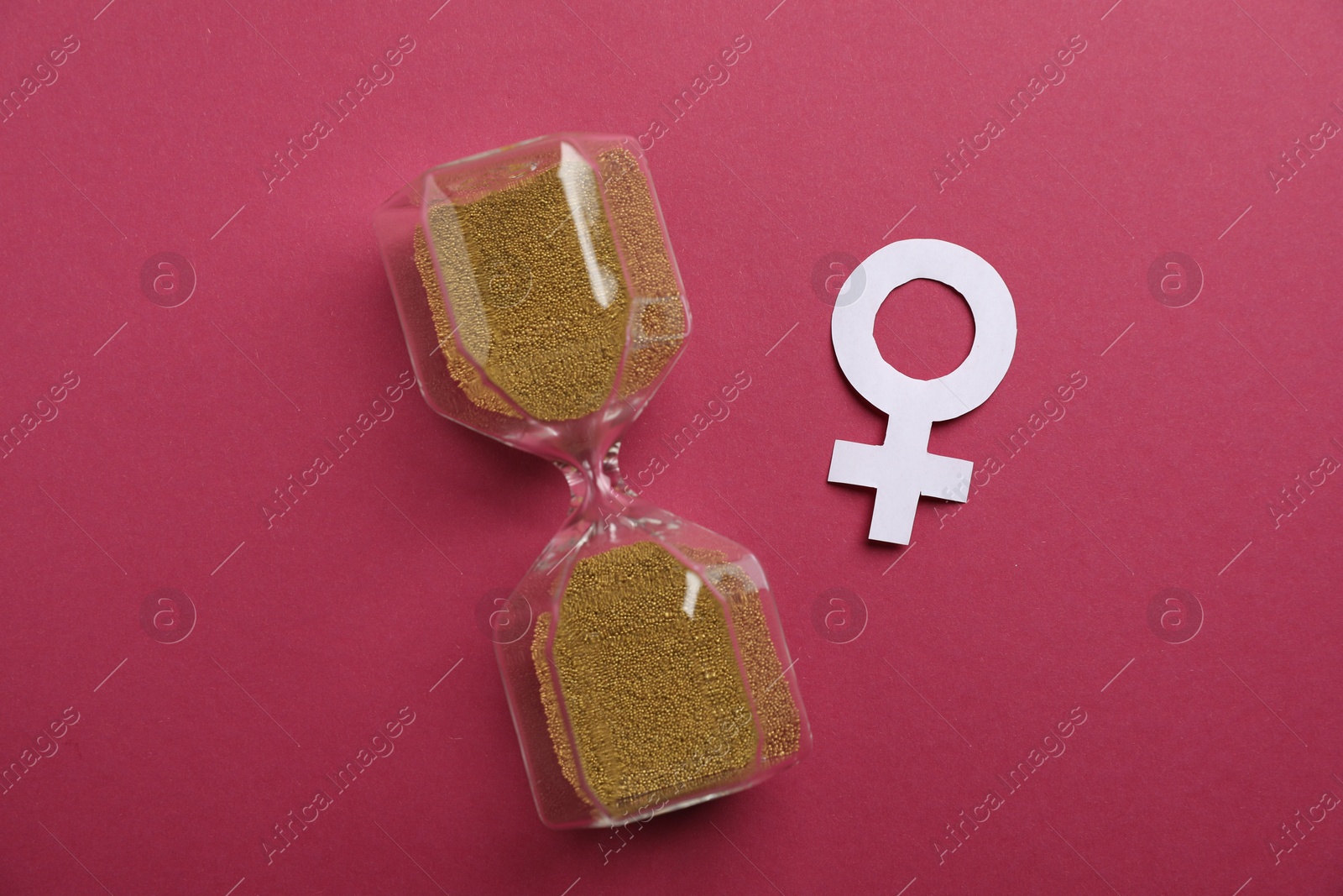 Photo of Menopause. Female gender symbol and hourglass on crimson background, top view