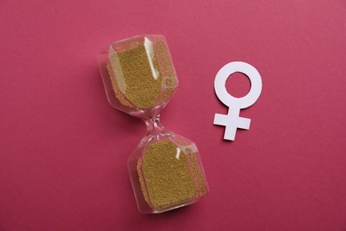Photo of Menopause. Female gender symbol and hourglass on crimson background, top view