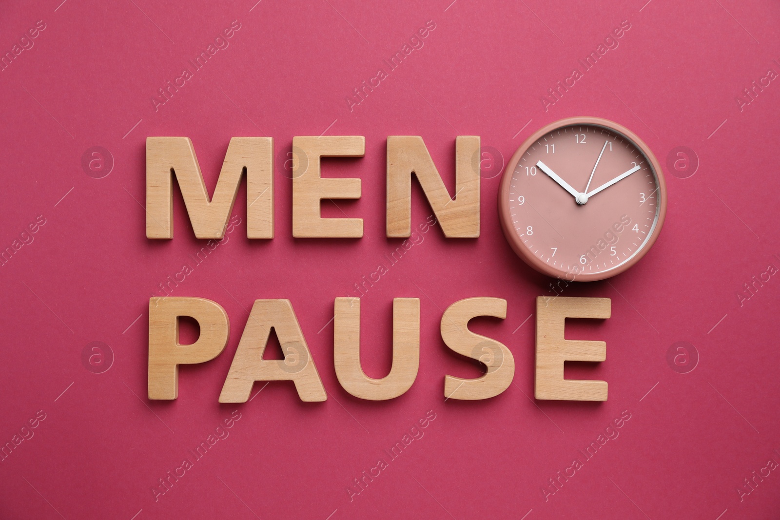 Photo of Word Menopause and alarm clock on crimson background, top view