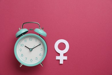 Photo of Menopause. Female gender symbol and alarm clock on crimson background, flat lay. Space for text