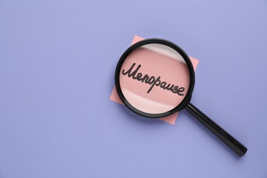 Photo of Magnifying glass over paper note with word Menopause on violet background, top view. Space for text