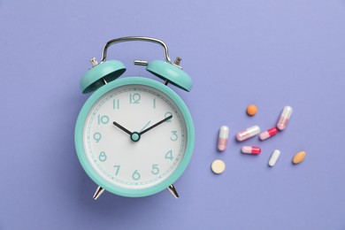 Photo of Menopause. Alarm clock and pills on violet background, flat lay