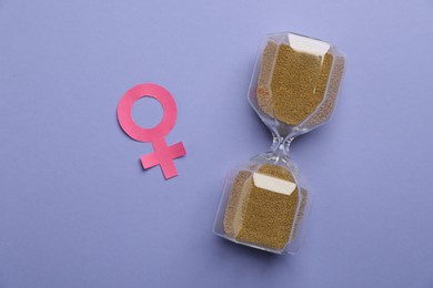 Photo of Menopause. Female gender symbol and hourglass on violet background, flat lay