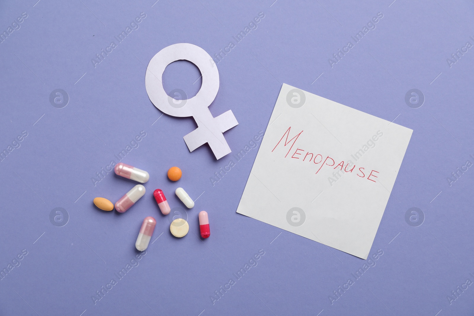 Photo of Paper note with word Menopause, female gender symbol and pills on violet background, flat lay