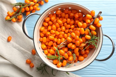 Photo of Fresh sea buckthorn berries in metal colander and leaves on light blue wooden table, flat lay