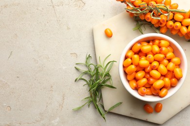 Photo of Fresh sea buckthorn berries in bowl and leaves on beige table, flat lay. Space for text