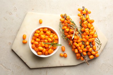 Photo of Fresh sea buckthorn berries in bowl and leaves on beige table, flat lay