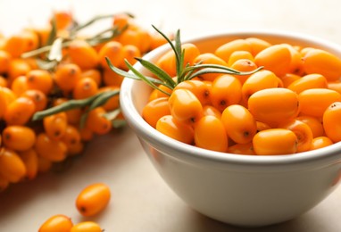 Photo of Fresh sea buckthorn berries in bowl and leaves on beige table, closeup