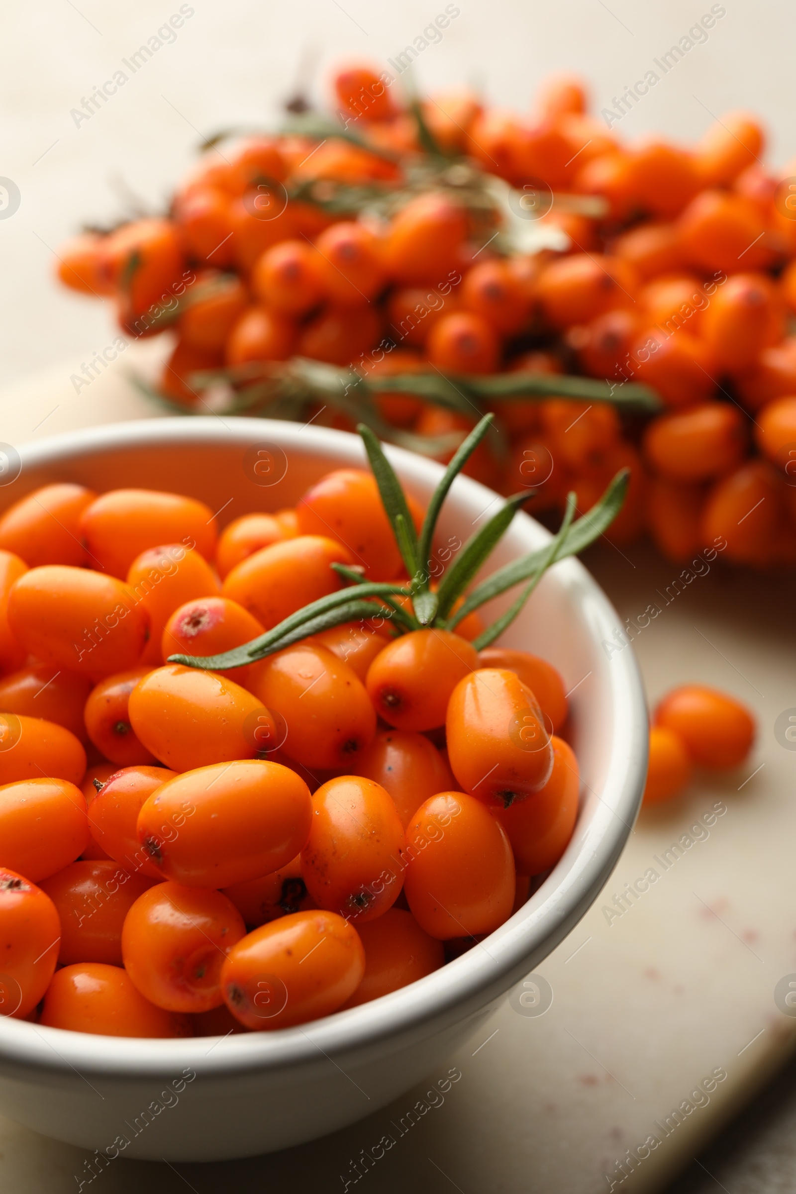 Photo of Fresh sea buckthorn berries in bowl and leaves on beige table, closeup