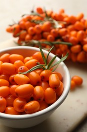 Photo of Fresh sea buckthorn berries in bowl and leaves on beige table, closeup