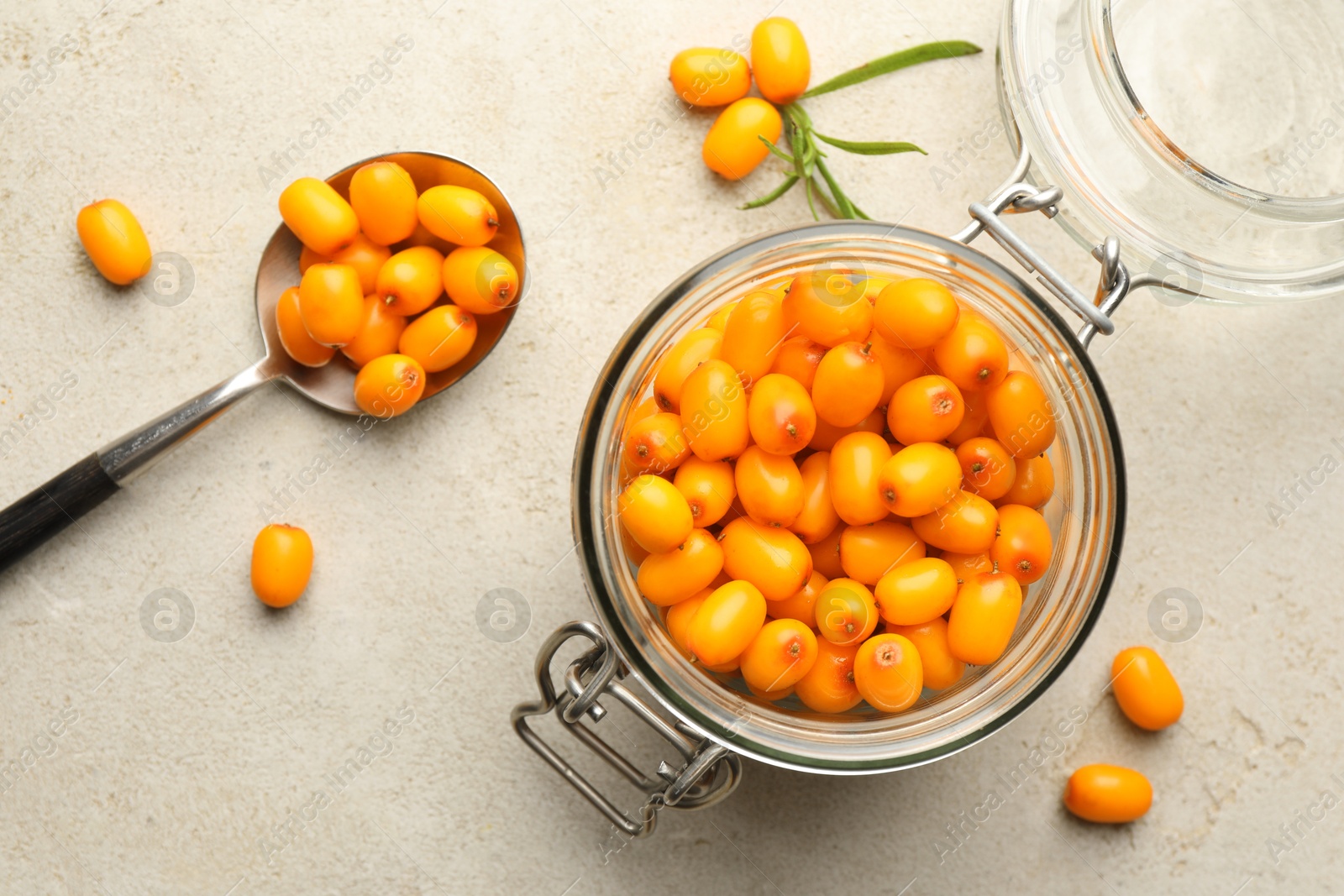 Fresh sea buckthorn berries in glass jar and leaves on beige table, flat lay Photo of Fresh sea buckthorn berries in glass jar and leaves on beige table, flat lay