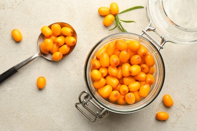 Photo of Fresh sea buckthorn berries in glass jar and leaves on beige table, flat lay