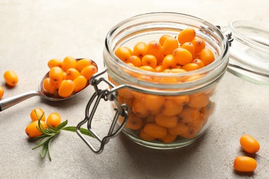 Photo of Fresh sea buckthorn berries in glass jar and leaves on beige table, closeup