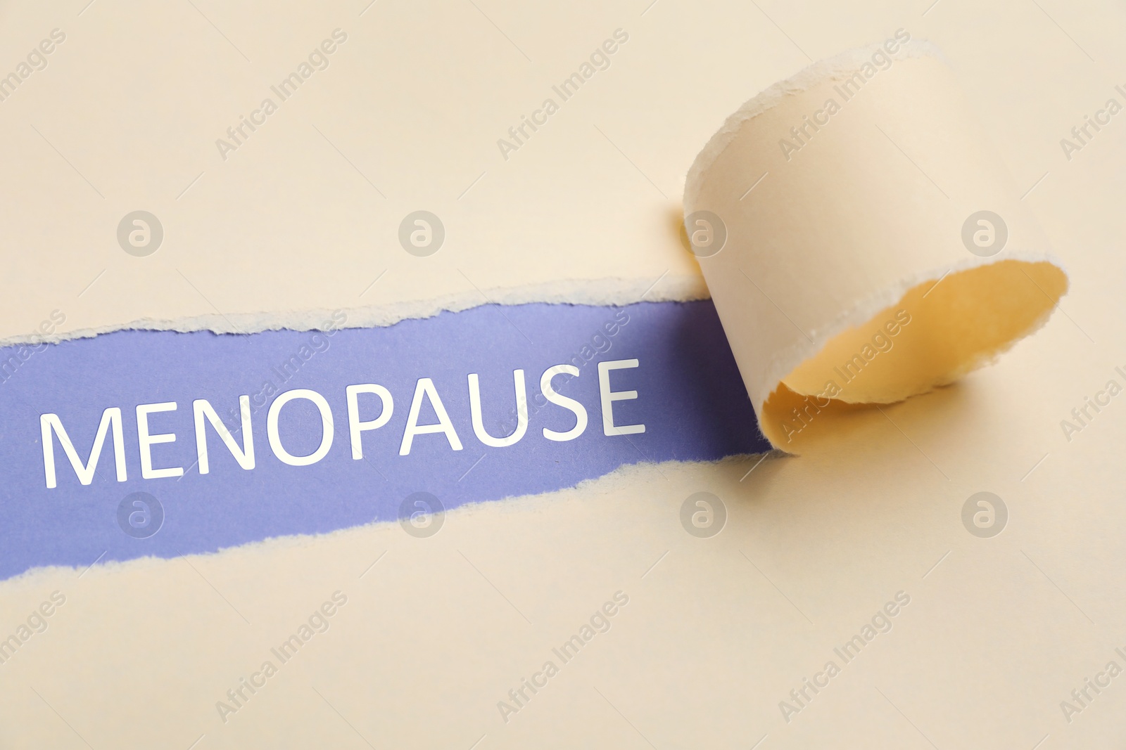 Photo of Word Menopause on violet background, view through hole in torn beige paper