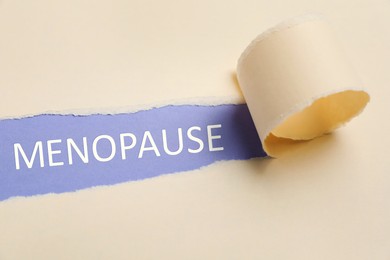 Photo of Word Menopause on violet background, view through hole in torn beige paper